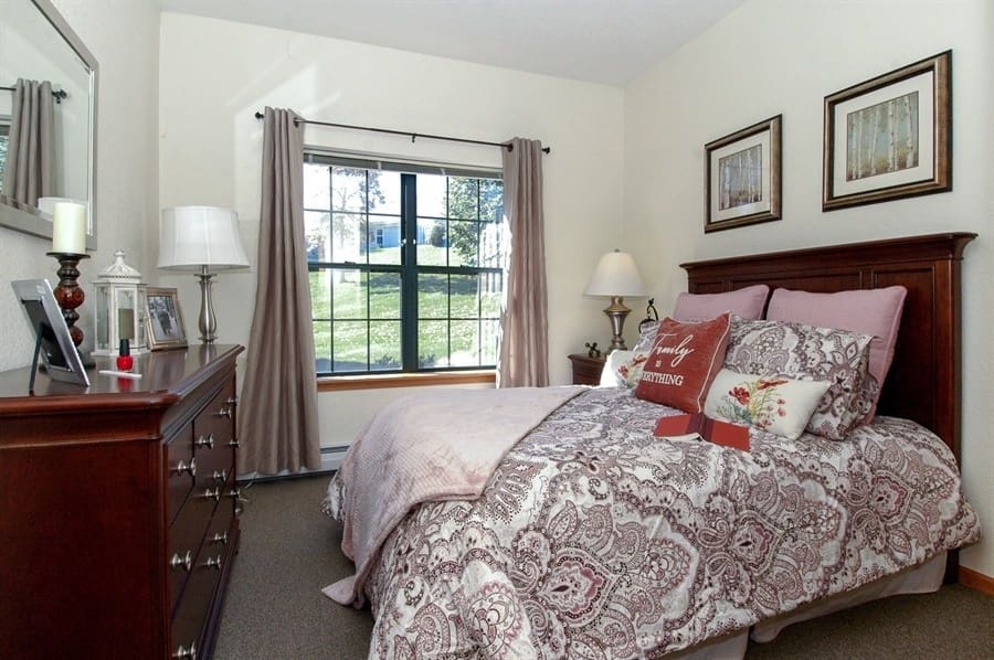 Bright and comfortable bedroom at Charter Senior Living of Madison, WI, featuring large window, soft bedding, and home-like decor
